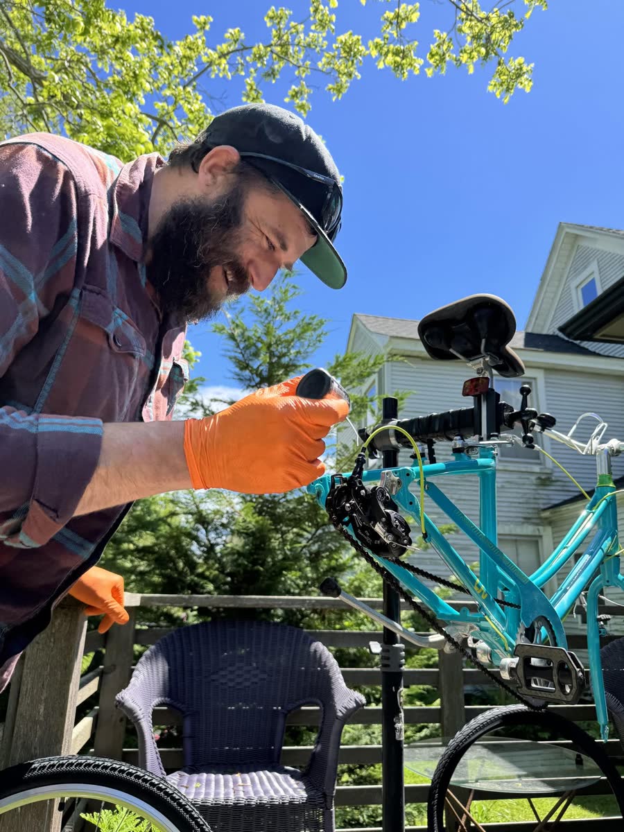 Dan working on a turquoise bicycle on a repair stand outdoors.